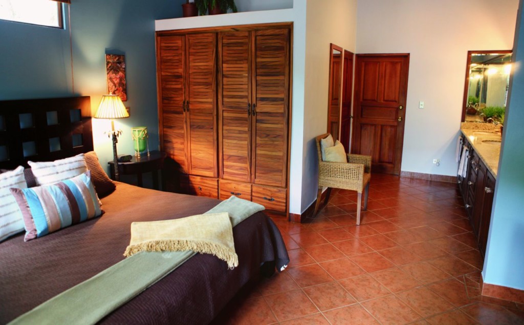 The master suite with its wooden wardrobe and bathroom door at Casa Colorado, a vacation rental home with a private pool in Tamarindo, Costa Rica