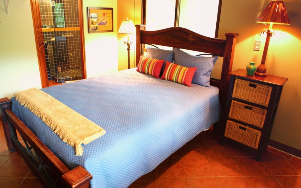 The queen bedroom with a carved wood bed and blue spread at Casa Colorado, a vacation rental home with a private pool in Tamarindo, Costa Rica