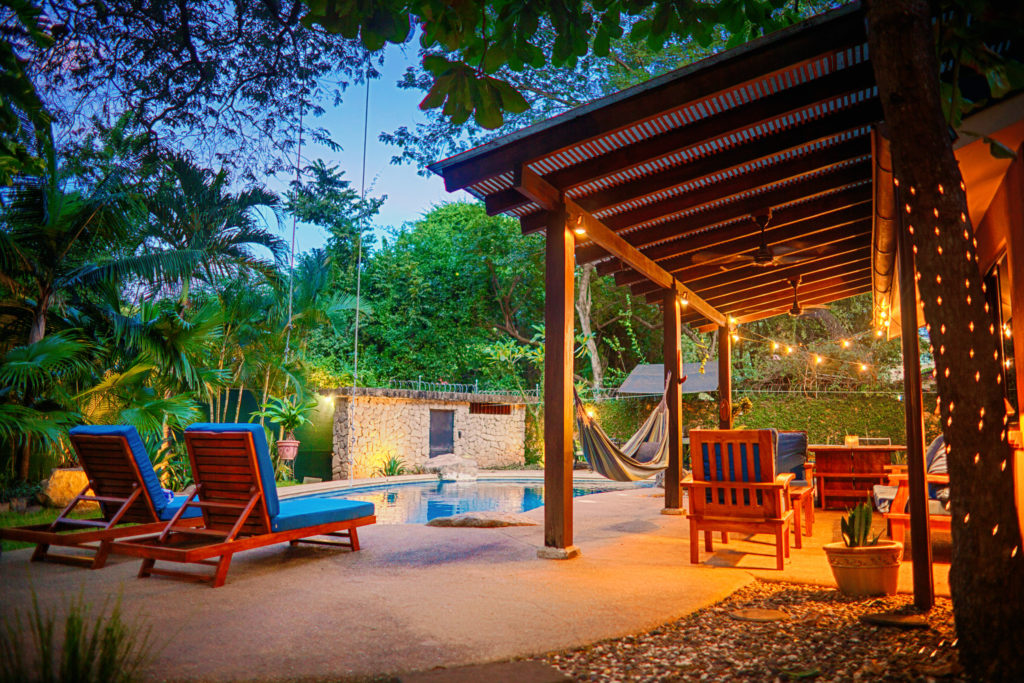 Sun loungers and the covered patio along the pool deck at dusk at Casa Colorado, a vacation rental home with a private pool in Tamarindo, Costa Rica