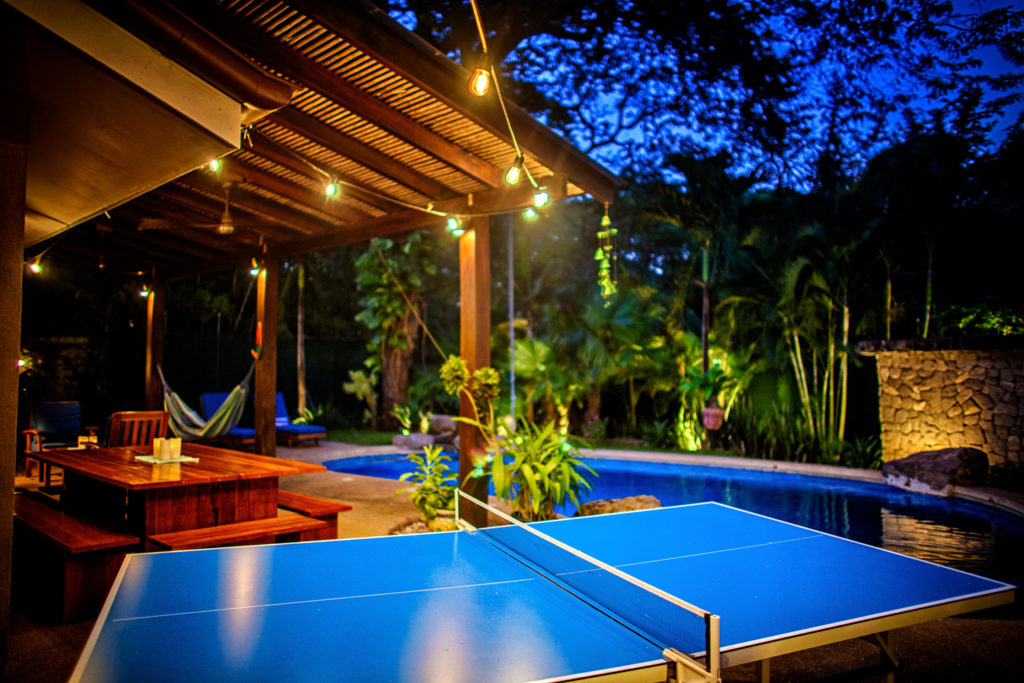 The ping pong table beside the lit pool at night at Casa Colorado, a vacation rental home with a private pool in Tamarindo, Costa Rica